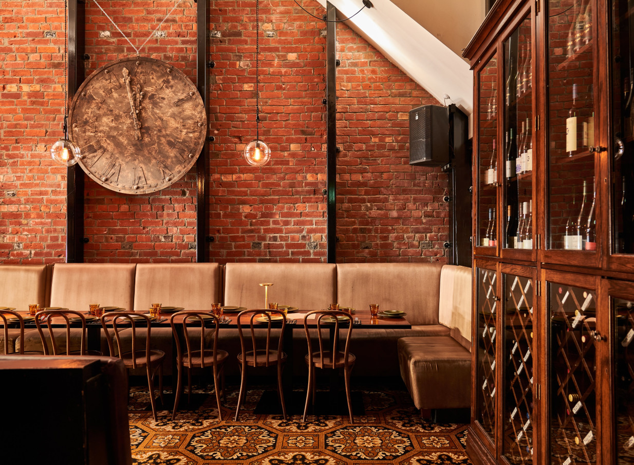 The Monday Room in Christchurch showcases a heritage dining room with exposed red brick, plush banquet seating, and a rustic clock.