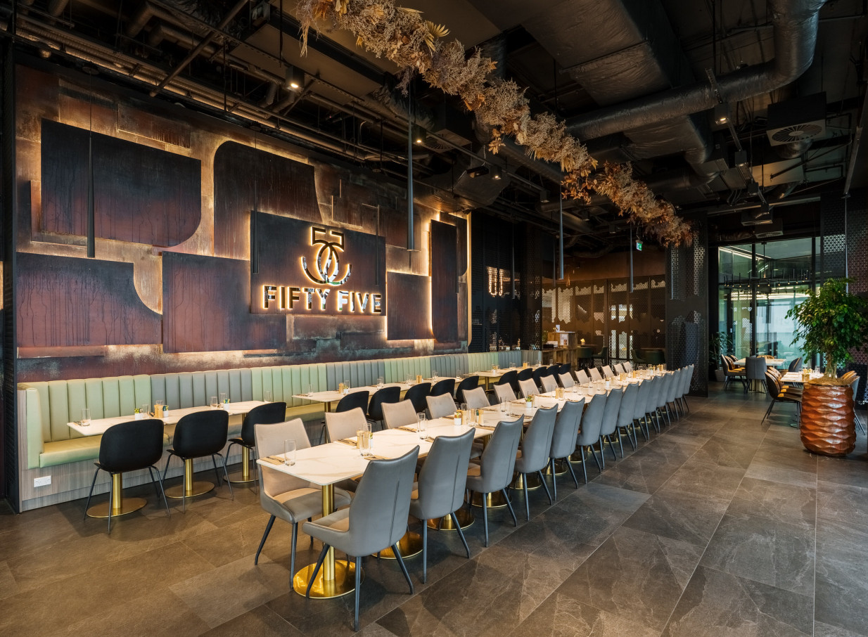 A chic, modern dining area at 55 Cafe in Auckland, featuring long tables, booth seating, and a prominent illuminated 'Fifty Five' sign.