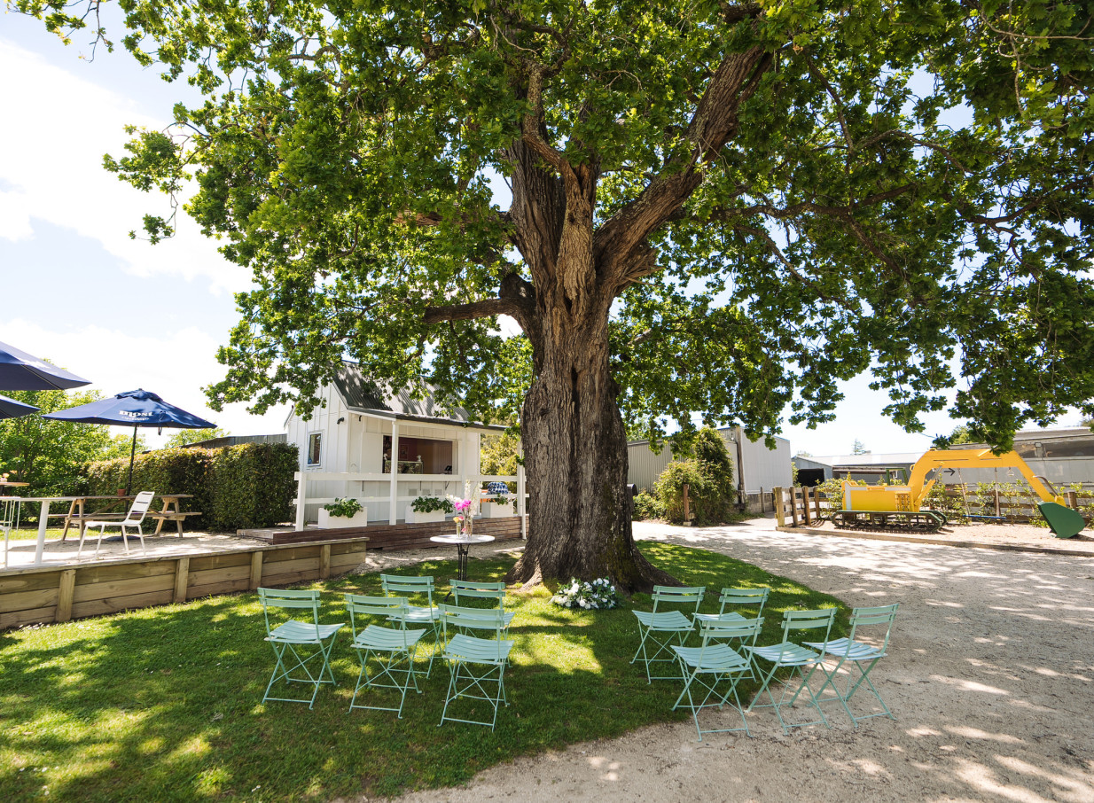 A rustic outdoor ceremony space at Farm House Cafe, Auckland, featuring a large tree and charming white villa.