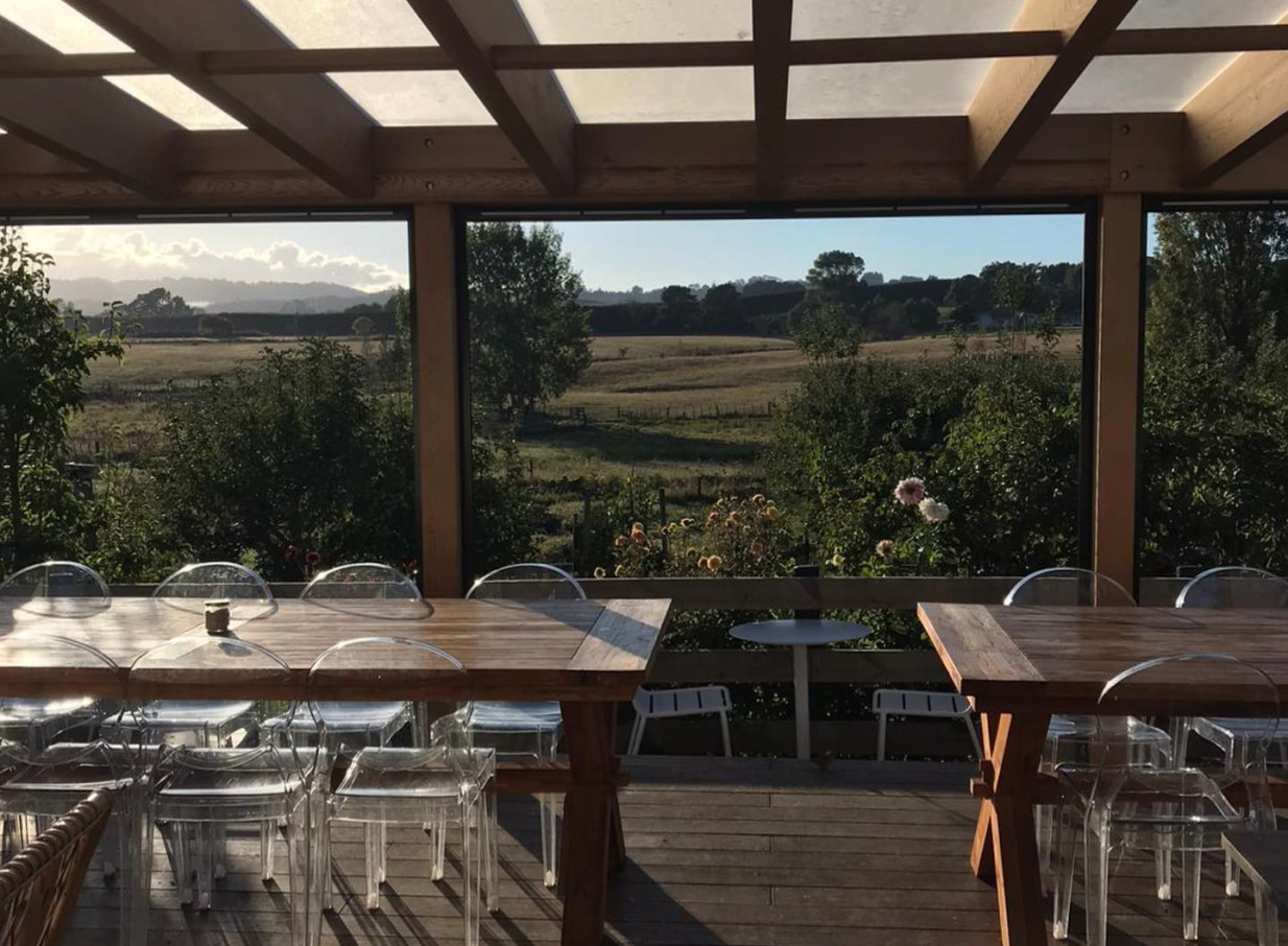 Enjoy outdoor dining at Farm House Cafe, Auckland, a charming villa with a rustic patio offering expansive views of Clevedon countryside.