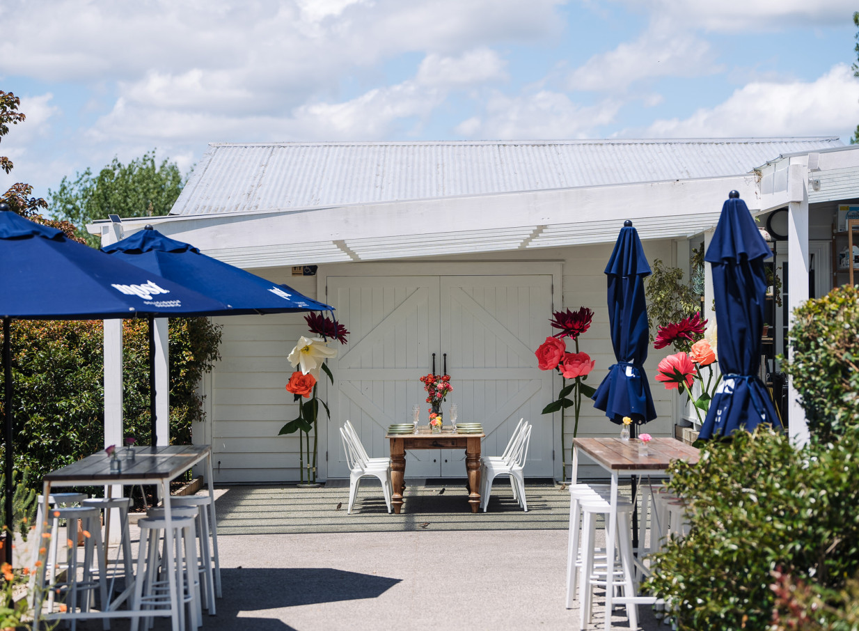 A charming farmhouse-style outdoor dining area at Farm House Cafe, Auckland, with set tables and decorative giant flowers.