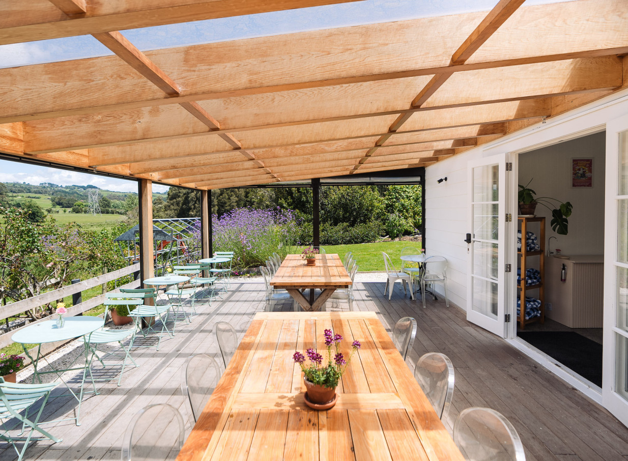 Farm House Cafe in Auckland's charming white villa offers a rustic outdoor dining space with wooden tables and panoramic countryside views.
