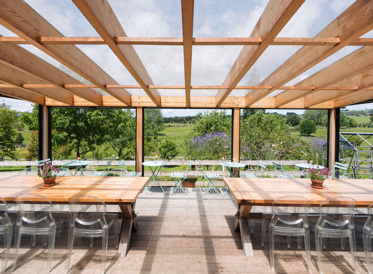 An outdoor dining terrace at Farm House Cafe, Auckland, features a rustic wooden pergola overlooking the picturesque countryside.