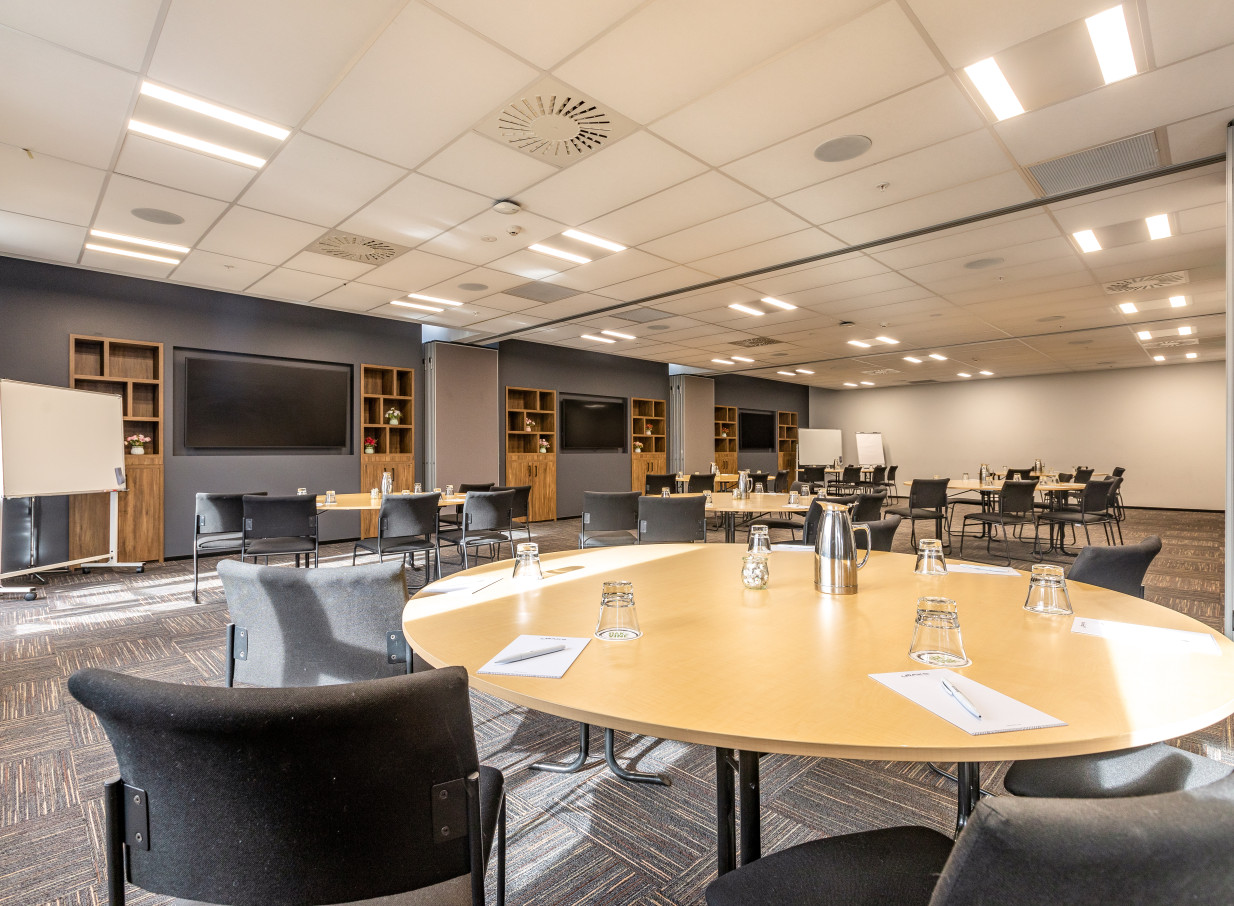 A contemporary conference room with round tables and AV displays at the modern Oaks Wellington Hotel.