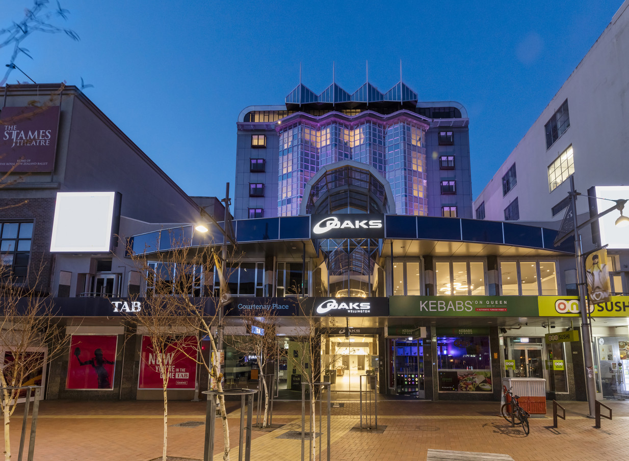 Exterior view of the contemporary Oaks Wellington Hotel in Wellington, featuring illuminated glass facades at night.