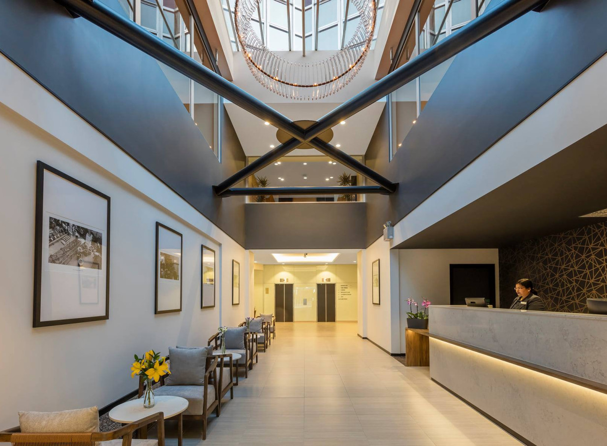 The contemporary and industrial-chic lobby of Oaks Wellington Hotel features a multi-story atrium, front desk, and comfortable seating.
