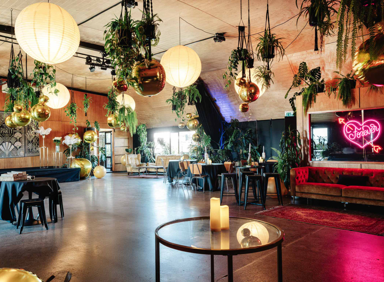 Evil Genius's Lair event space in Christchurch features a rustic and elegant setting adorned with lush greenery and warm, ambient lighting.