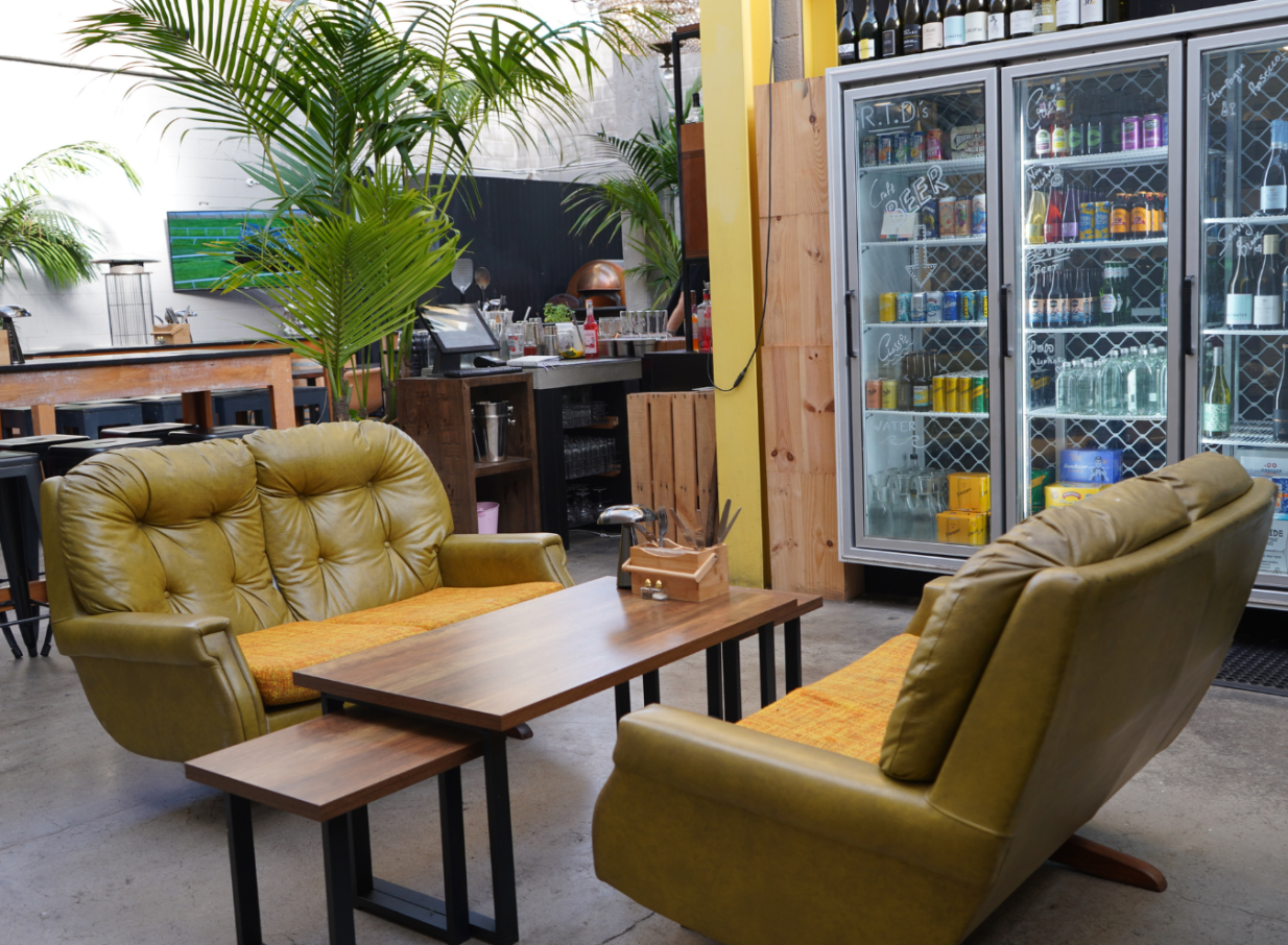 A cozy lounge area with olive-green seating and plants, reflecting Orakei Local's stylish, laid-back vibe in Auckland.