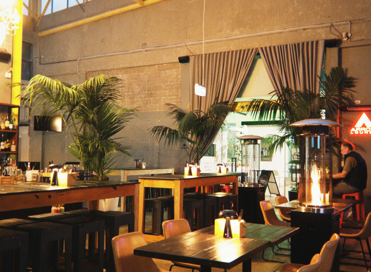 This industrial-chic dining room with warm lighting, concrete walls, and palm plants is Orakei Local in Auckland.