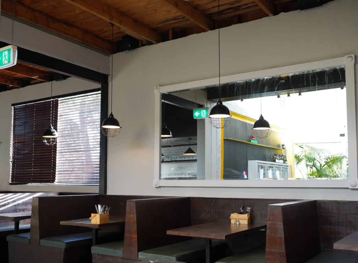 This rustic industrial dining area at Orakei Local, Auckland, features dark wooden booths, exposed beam ceilings, and pendant lights.