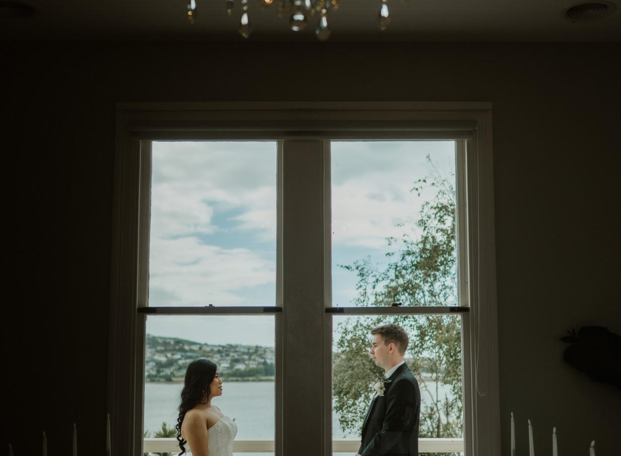 A couple pauses by a window in the historic Victorian Gear Homestead, Wellington, overlooking a scenic view.