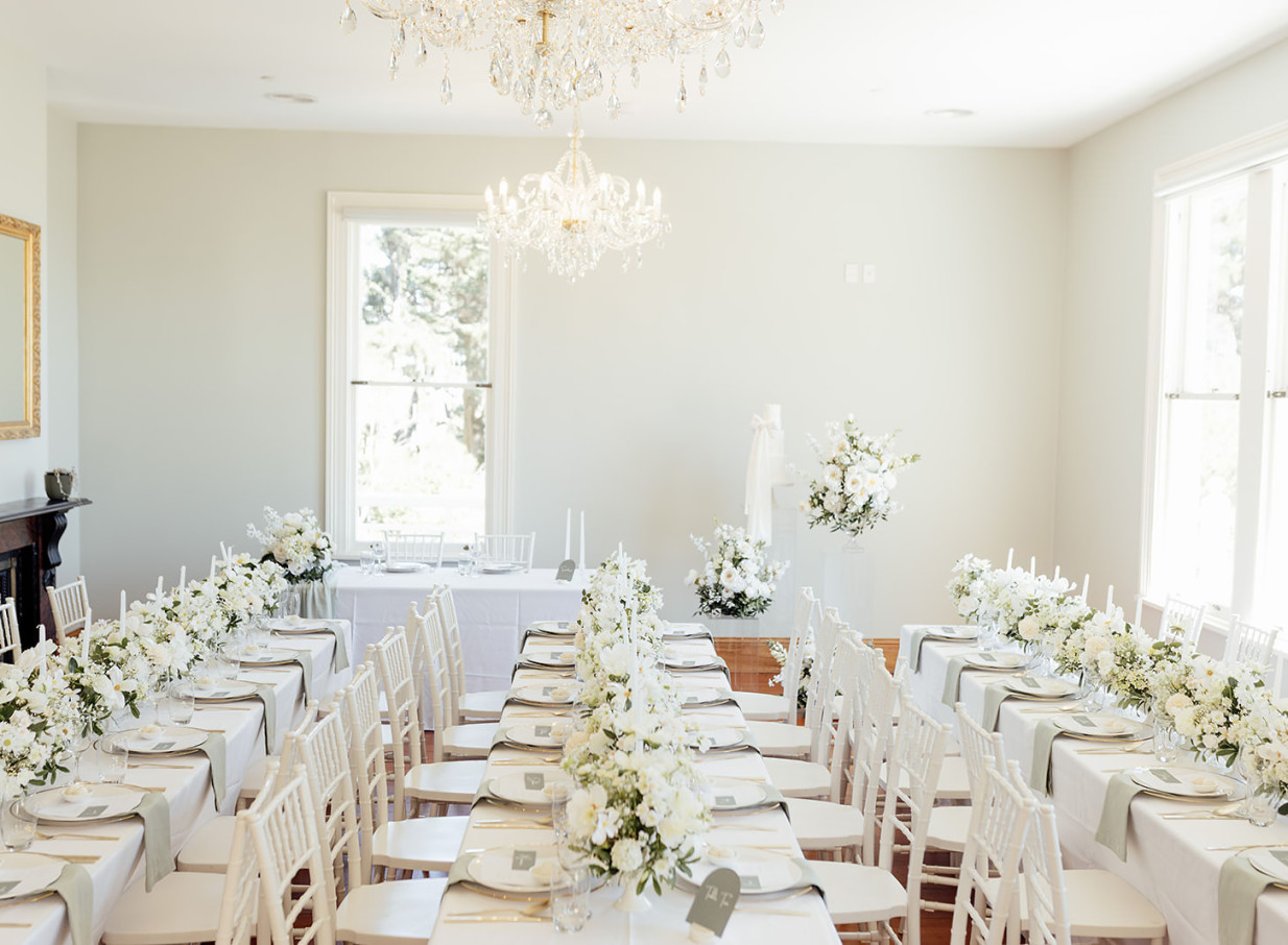 An elegant wedding reception dining room with white florals and chandeliers at the historic Victorian-style Gear Homestead in Wellington.