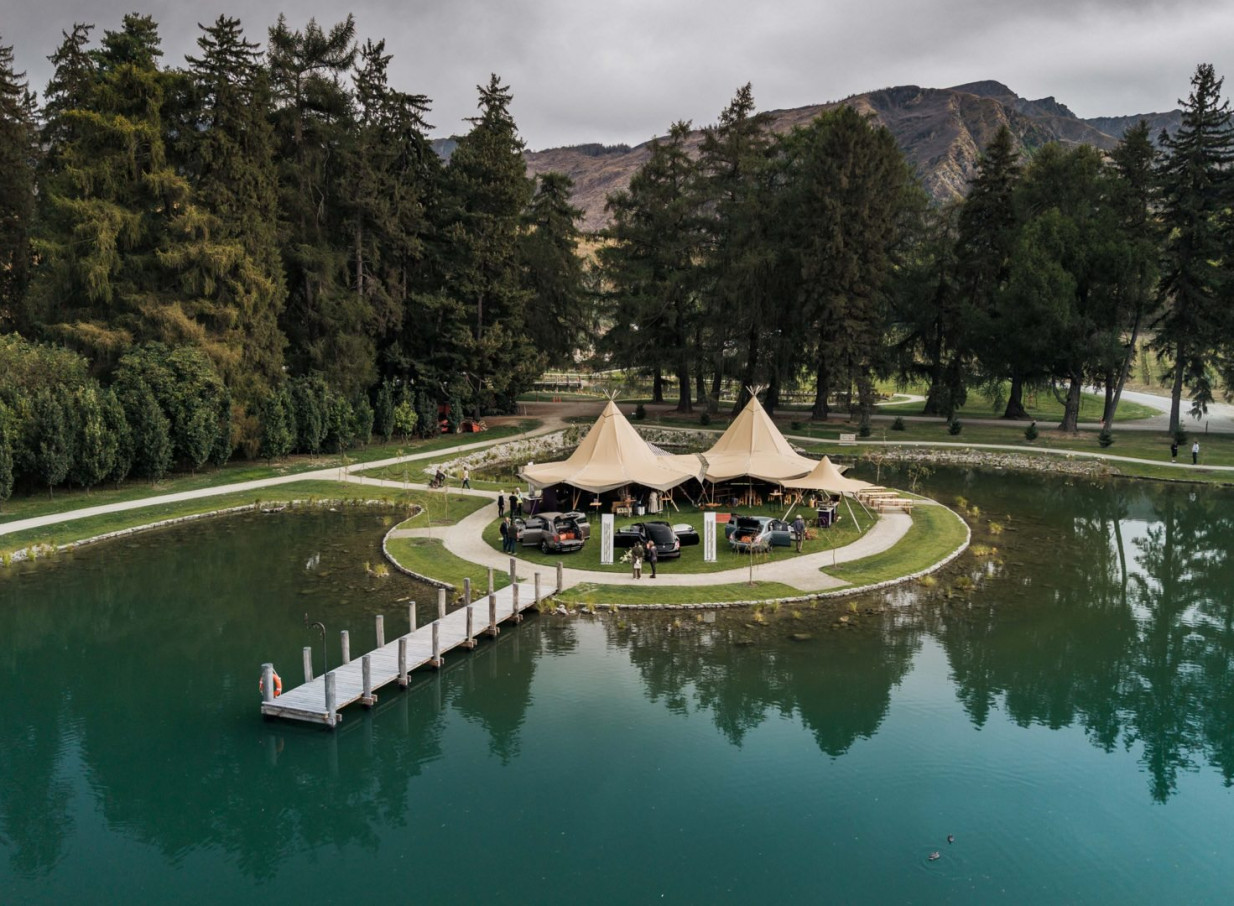 Ayrburn Queenstown's elegant outdoor event features marquees on a pond island with a scenic jetty.