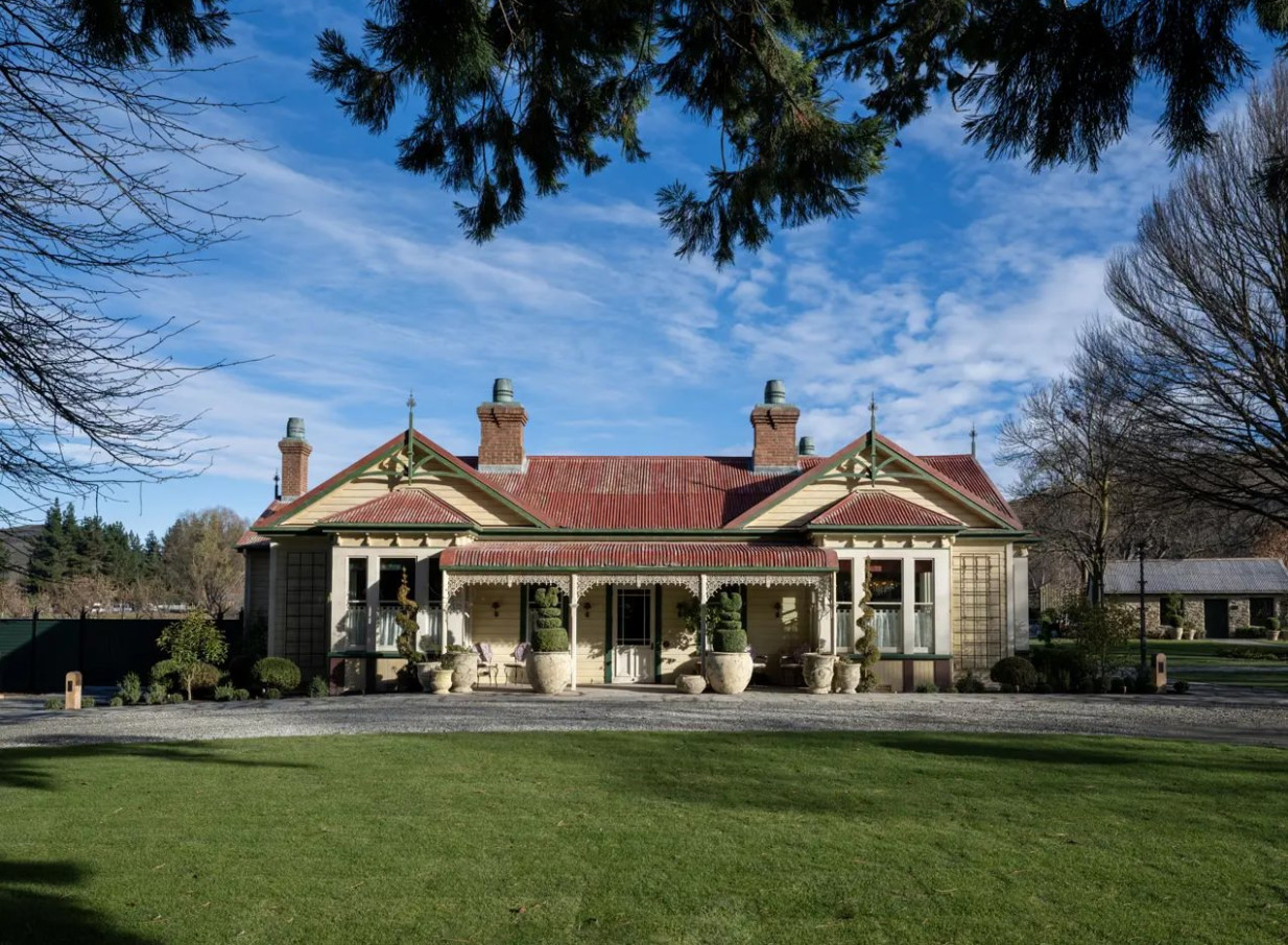 An ornate colonial-Victorian homestead with a red roof at Ayrburn in Queenstown, nestled amidst a green lawn.