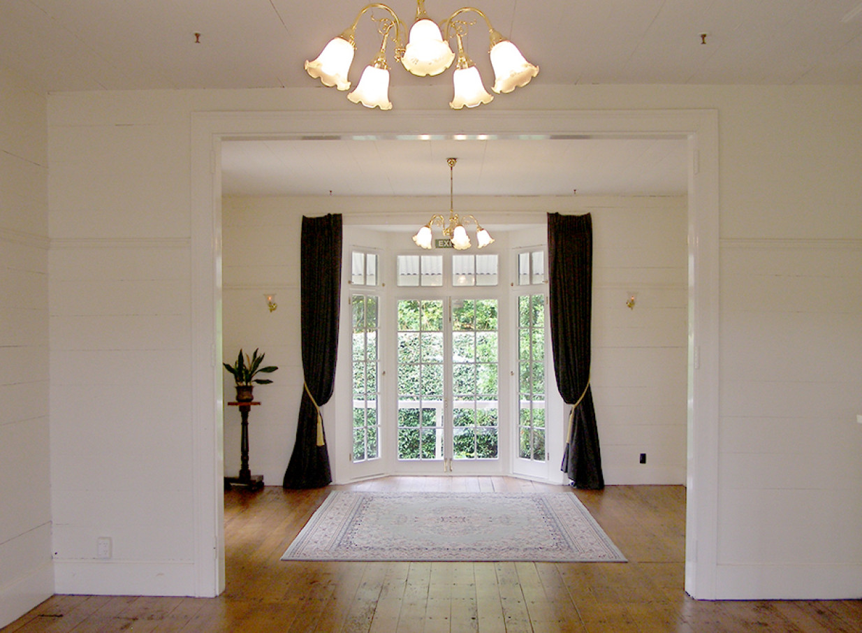 A brightly lit reception room with large bay windows in the historic Bell House at Howick Historical Village, Auckland.