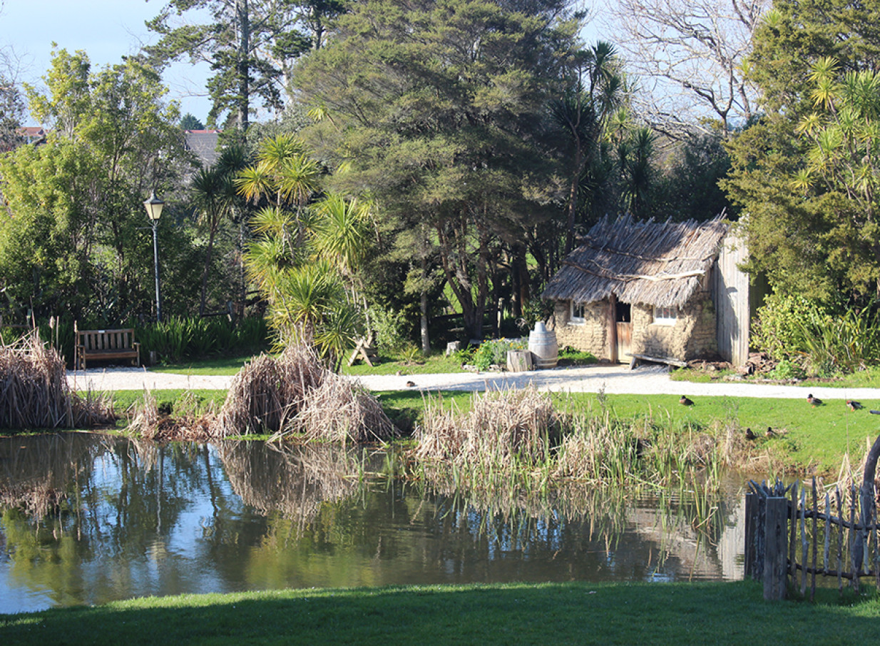 A scenic pond by a thatched-roof colonial cottage at the Howick Historical Village in Auckland.