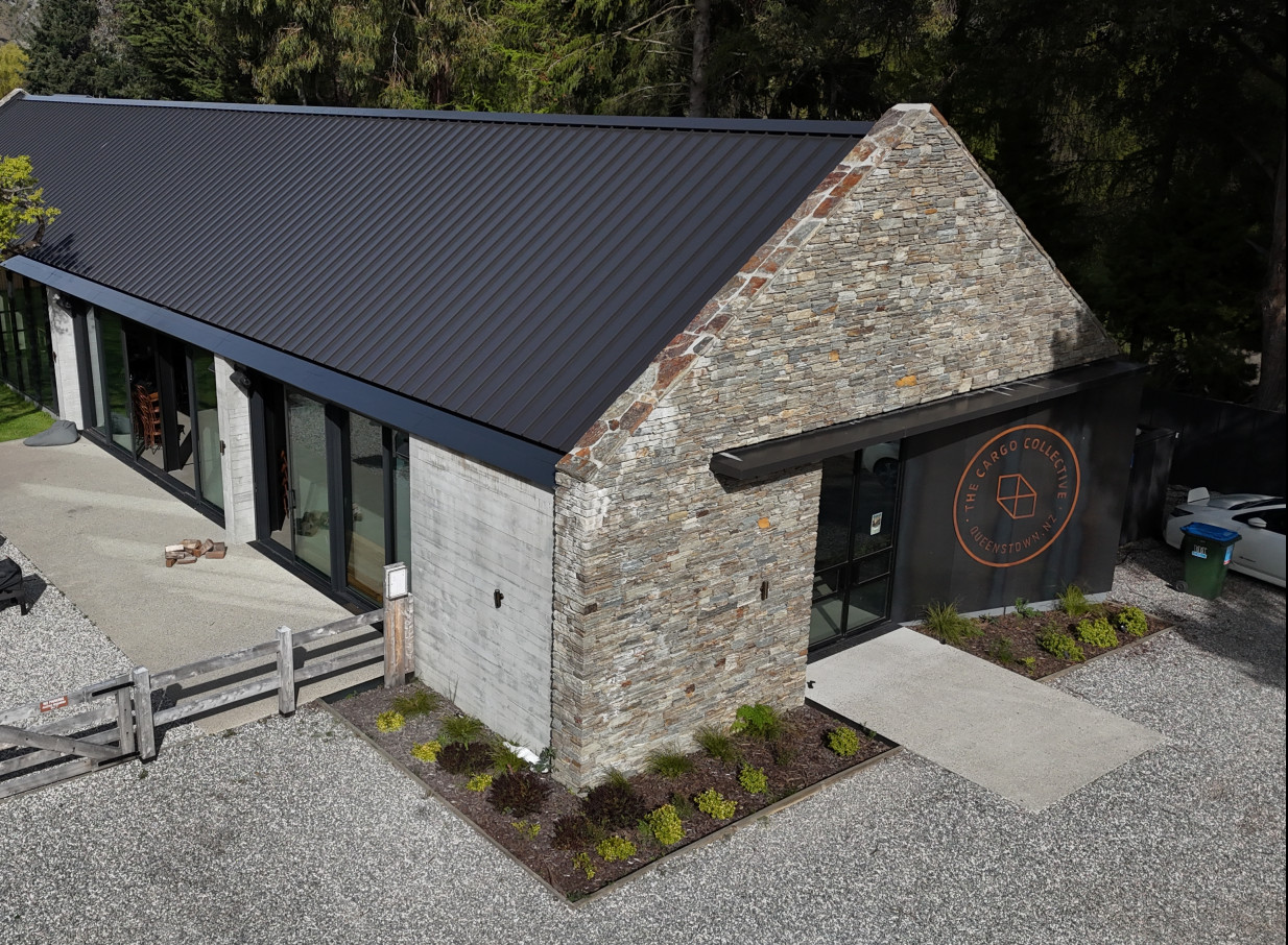 The rustic-modern stone and glass exterior of The Cargo Collective Brew Hall in Queenstown features an inviting gravel courtyard.