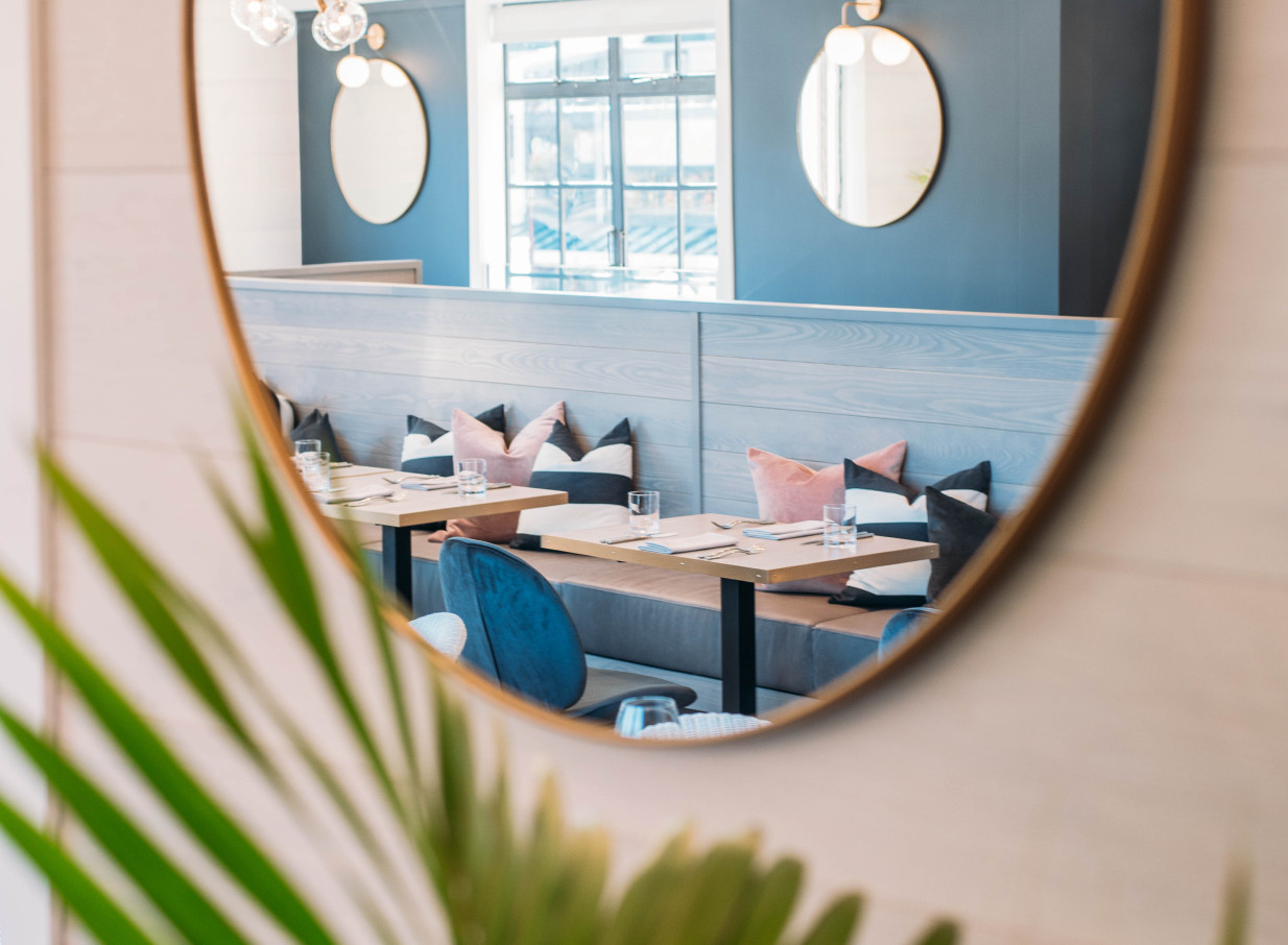 A chic dining area with modern nautical-themed booth seating, stylish mirrors, and colorful pillows at Boardwalk Queenstown.