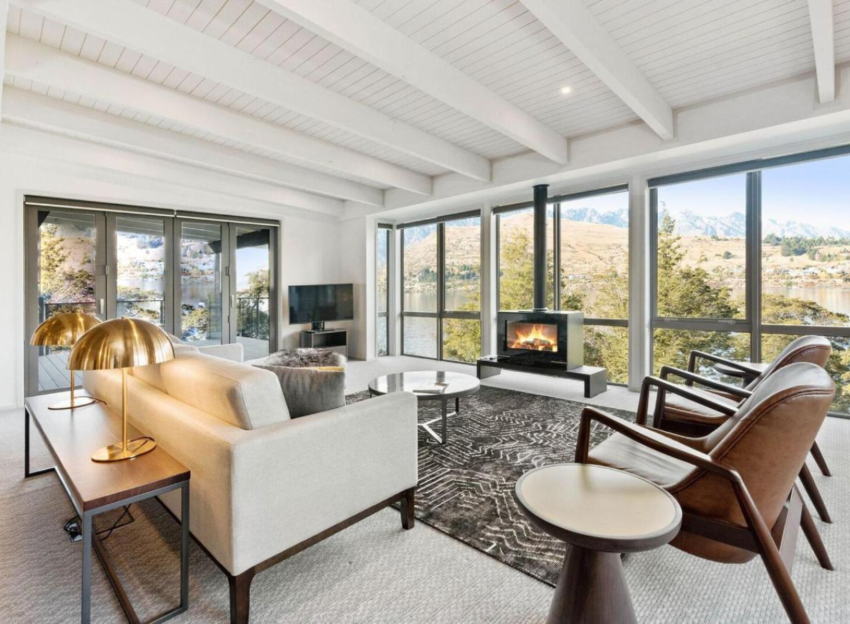 A modern alpine-style lounge at The Rees Hotel, Queenstown, featuring a fireplace and stunning views of Lake Wakatipu and mountains.