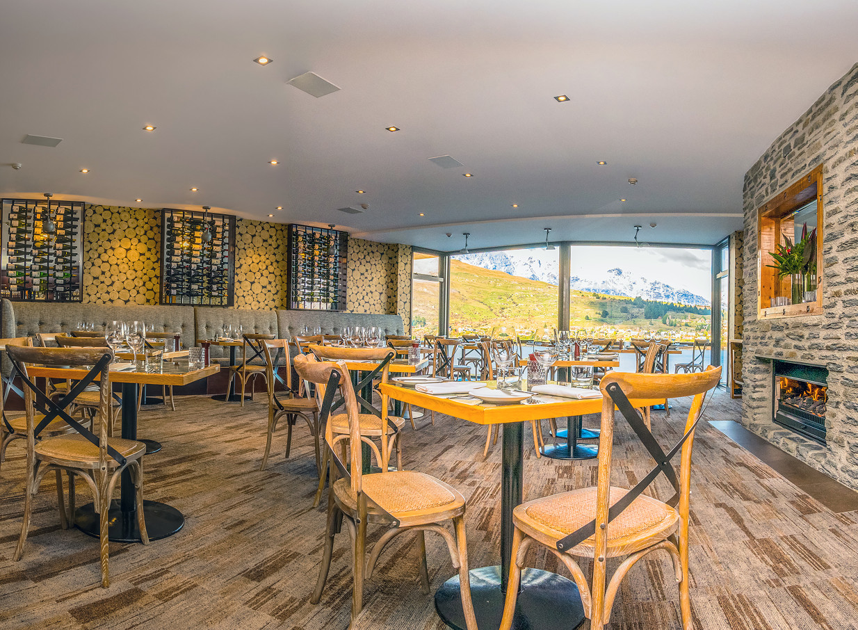 Sophisticated dining at The Rees Hotel, Queenstown, offers modern alpine style, a fireplace, and panoramic lake and mountain views.