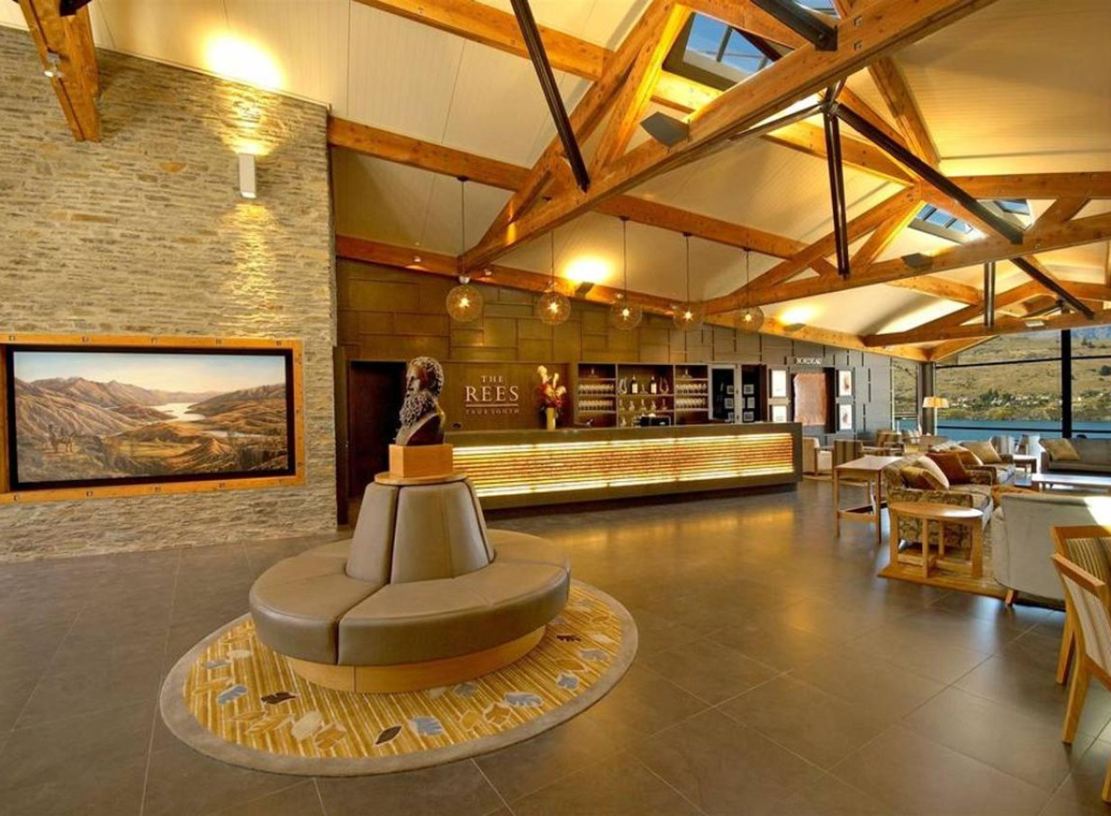 The contemporary alpine lodge lobby at The Rees Hotel Queenstown features exposed timber beams and stone walls.