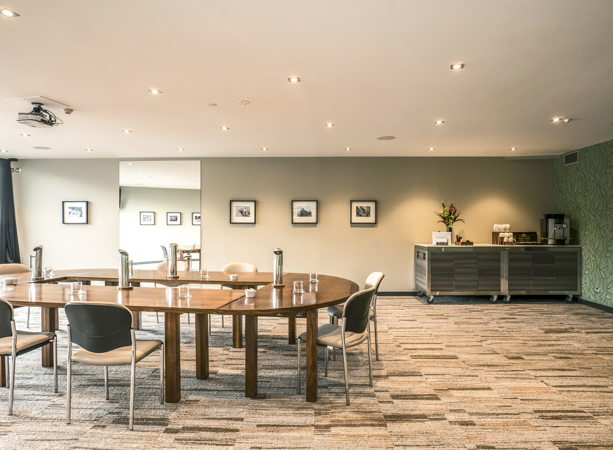 A sophisticated meeting room at The Rees Hotel Queenstown, with modern U-shaped tables and a refreshment station, ideal for events.