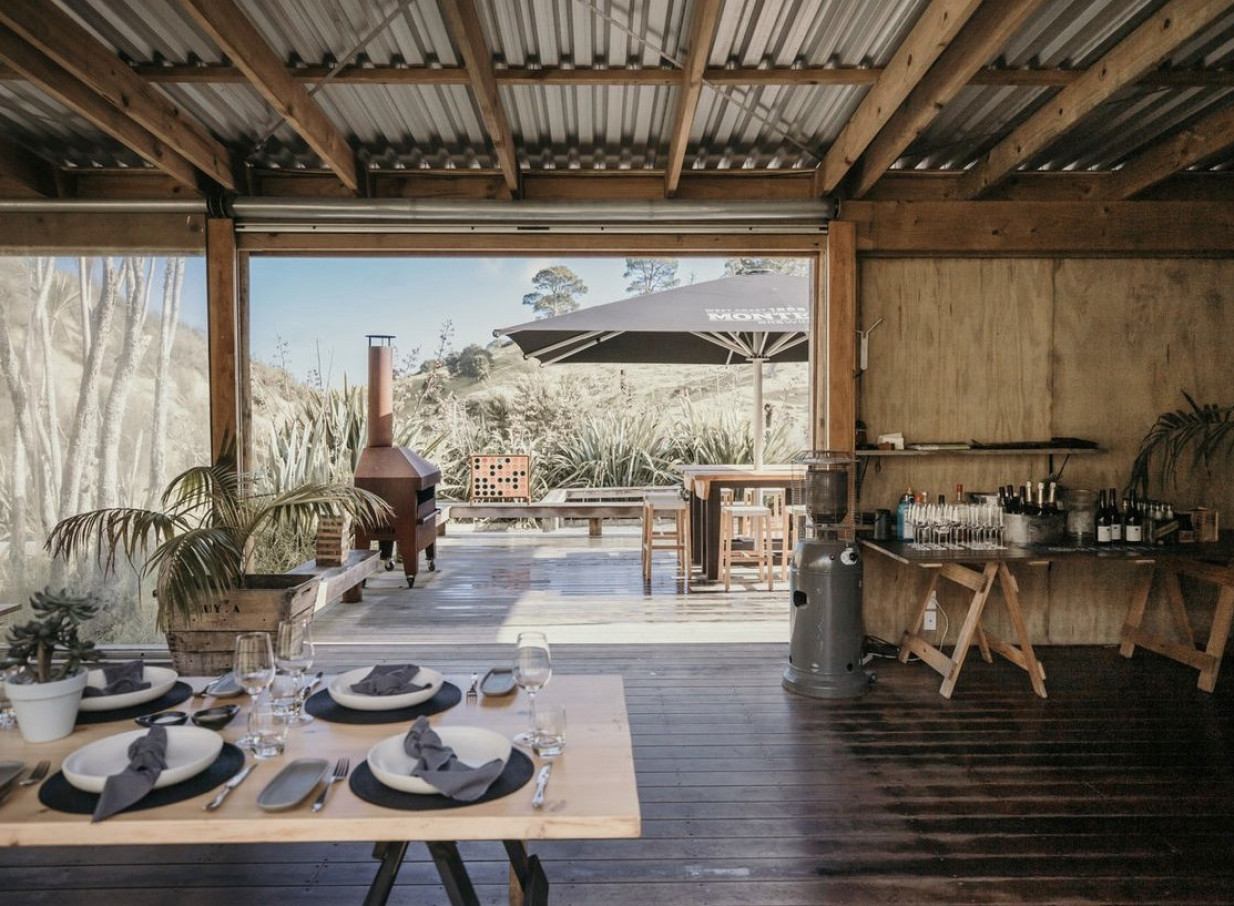 A modern-rustic outdoor dining setting with exposed timber and panoramic views at Kauri Bay in Auckland.