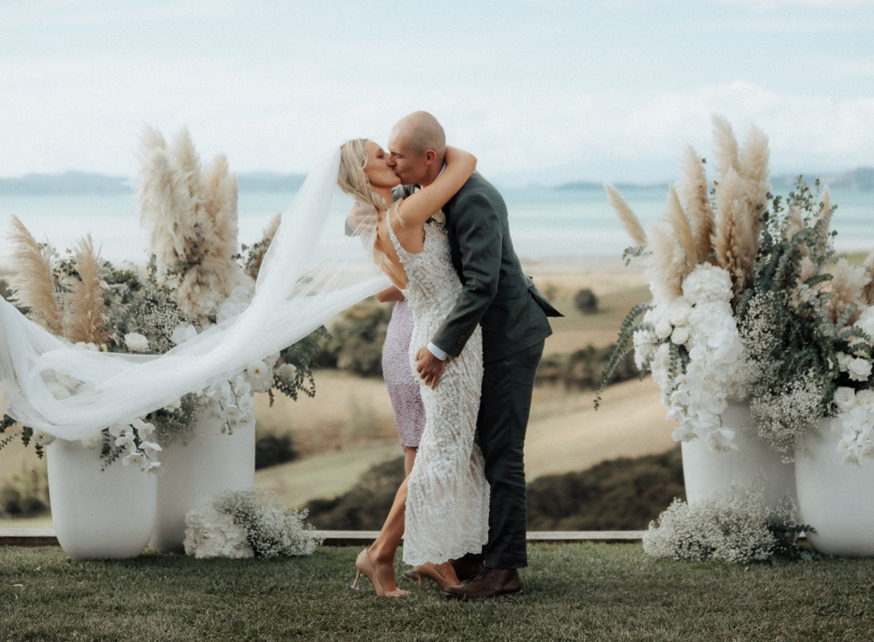 A couple kisses during their luxury-meets-nature outdoor ceremony at Kauri Bay, Auckland, overlooking the Hauraki Gulf.