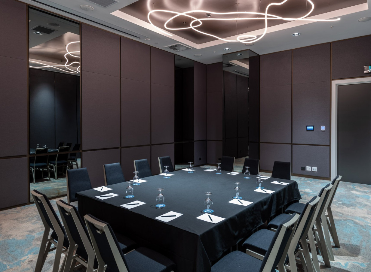 A modern meeting room at Four Points by Sheraton Auckland, featuring a large square table and unique abstract lighting.