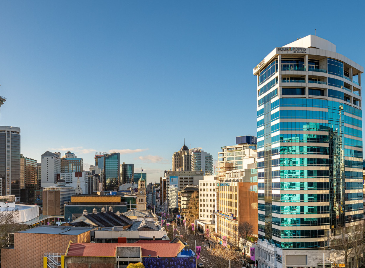 A contemporary 20-story Four Points by Sheraton Auckland hotel, with a distinctive blue-glass facade, stands prominently in the city skyline.