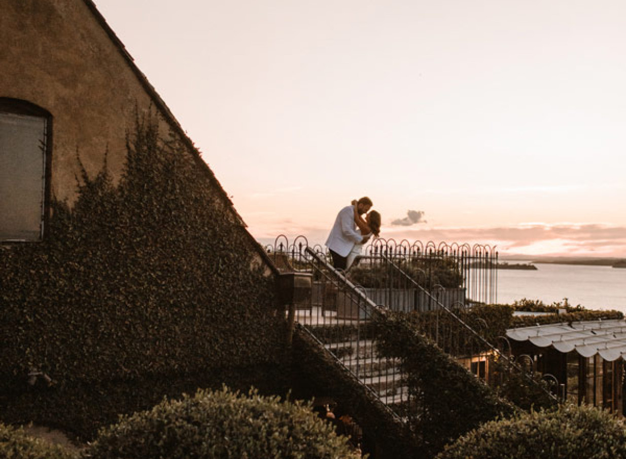 A couple shares a moment on the outdoor stairs of Mudbrick's Tuscan-inspired estate on Waiheke Island.