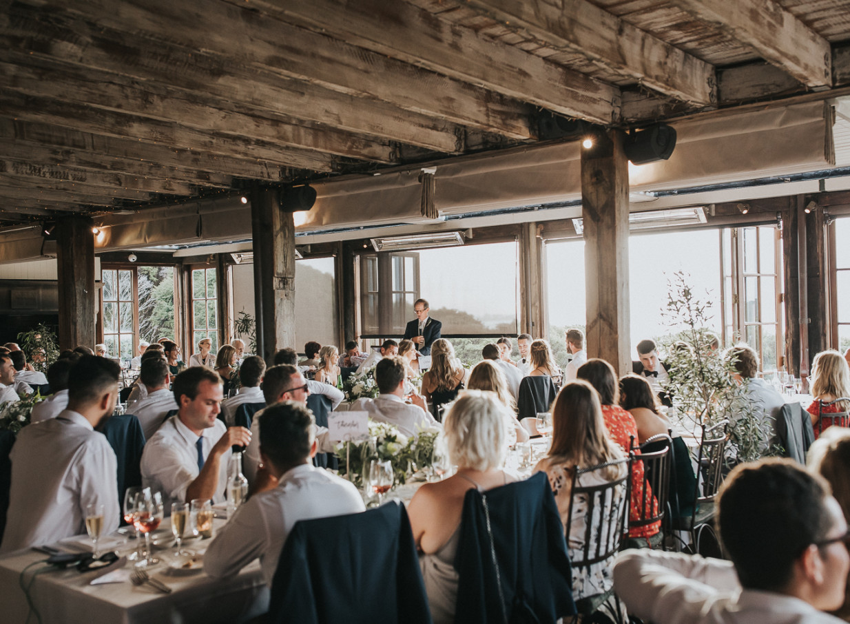 A wedding reception at Mudbrick's rustic-elegant mudbrick venue on Waiheke Island, with exposed beams and large windows.