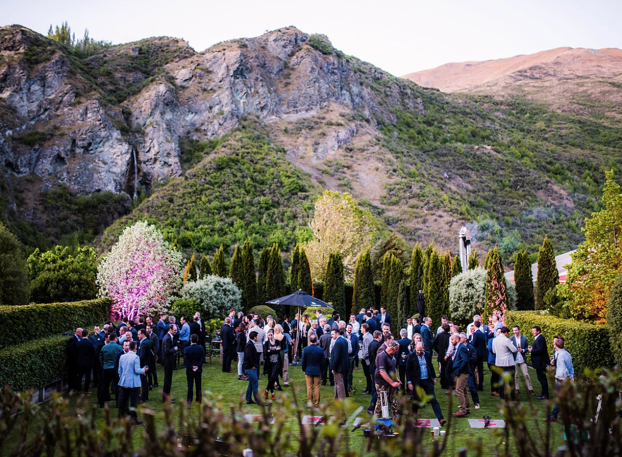 Guests gather in the beautiful gardens of Winehouse, a historic Queenstown homestead, surrounded by rugged mountains.