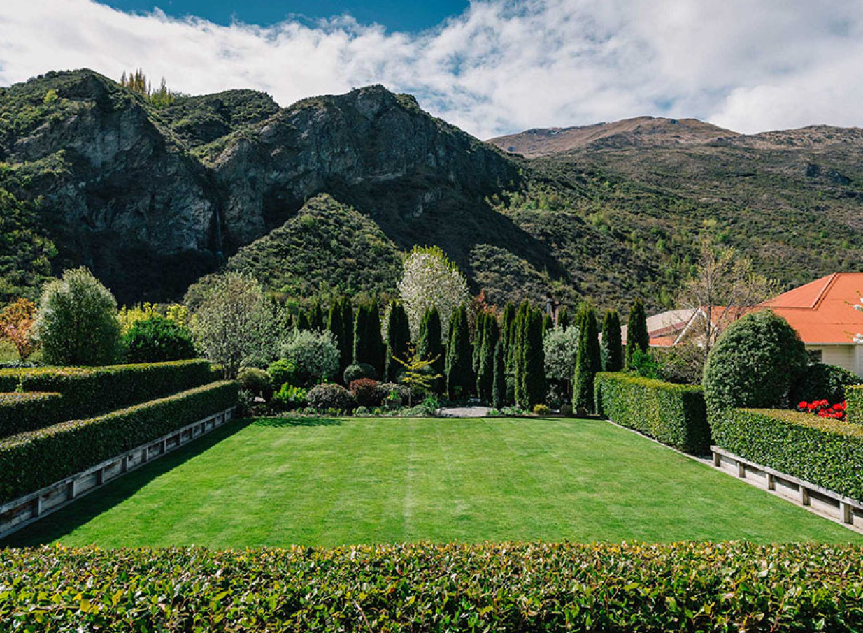 The Winehouse in Queenstown presents a manicured garden lawn for events, framed by lush trees and majestic mountains.