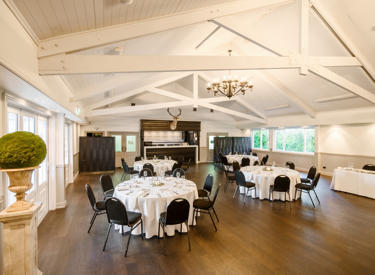 An elegant, Mediterranean-inspired event space at Bracu Estate in Auckland, featuring round tables and exposed white ceiling beams.