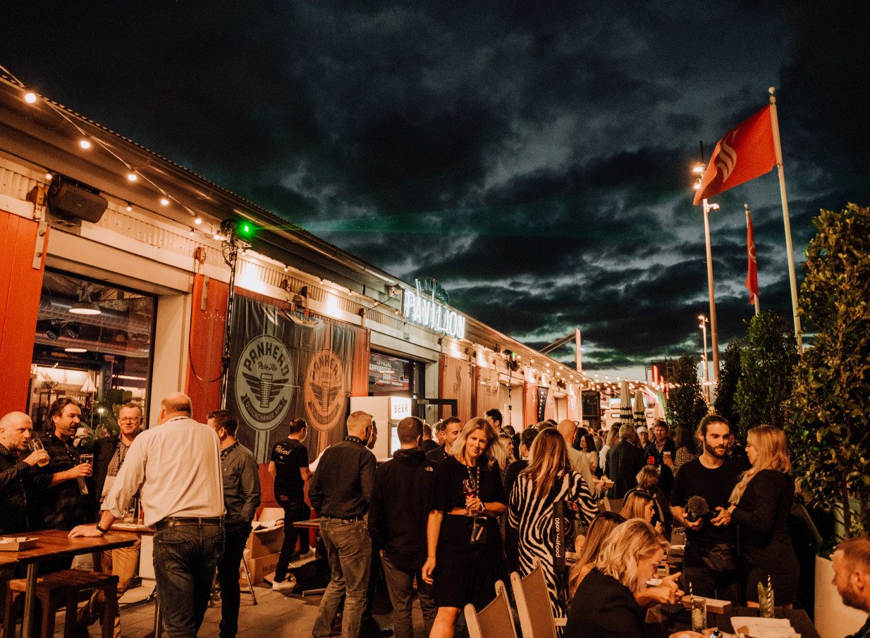 A lively outdoor evening gathering at the modern-industrial Wynyard Pavilion on Auckland's waterfront.