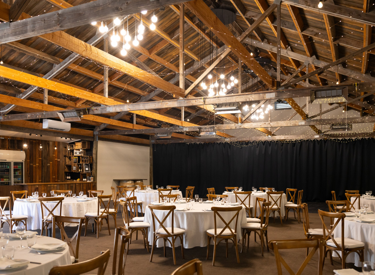 This rustic-chic event space, featuring exposed wooden beams and set dining tables, is located at Larcomb Vineyard, Christchurch.