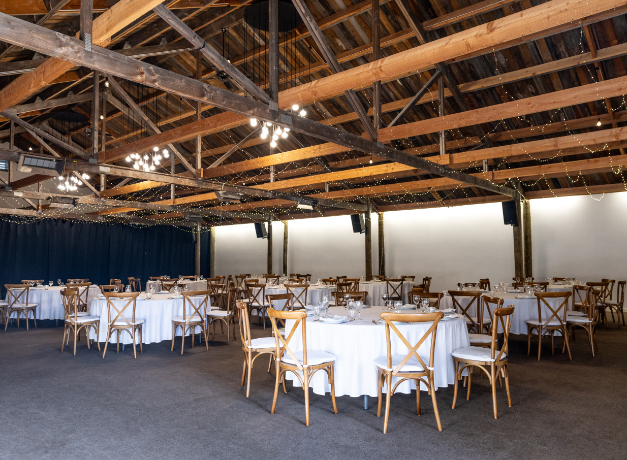 A rustic-styled barn event space at Larcomb Vineyard, Christchurch, features exposed wooden beams, fairy lights, and set tables.