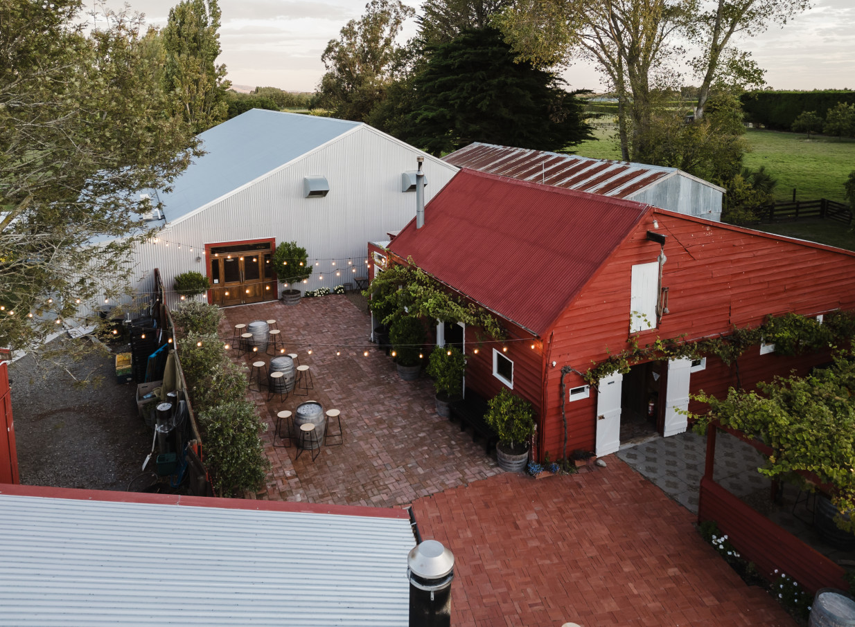 Larcomb Vineyard's rustic outdoor courtyard in Christchurch features string lights and barrel tables, ideal for elegant mingling.