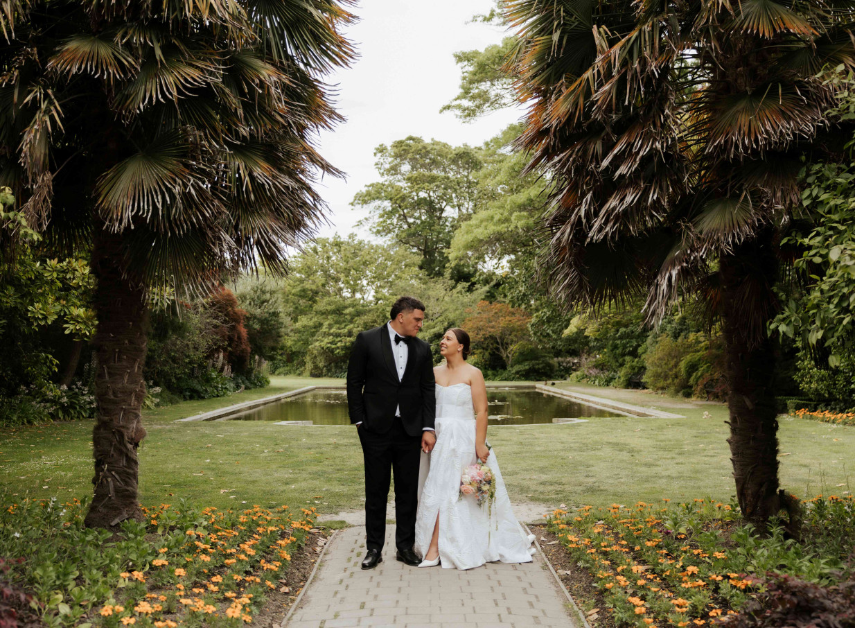 A wedding couple poses by the tranquil lily pond within the elegant landscaped gardens of Mona Vale Homestead, Christchurch.