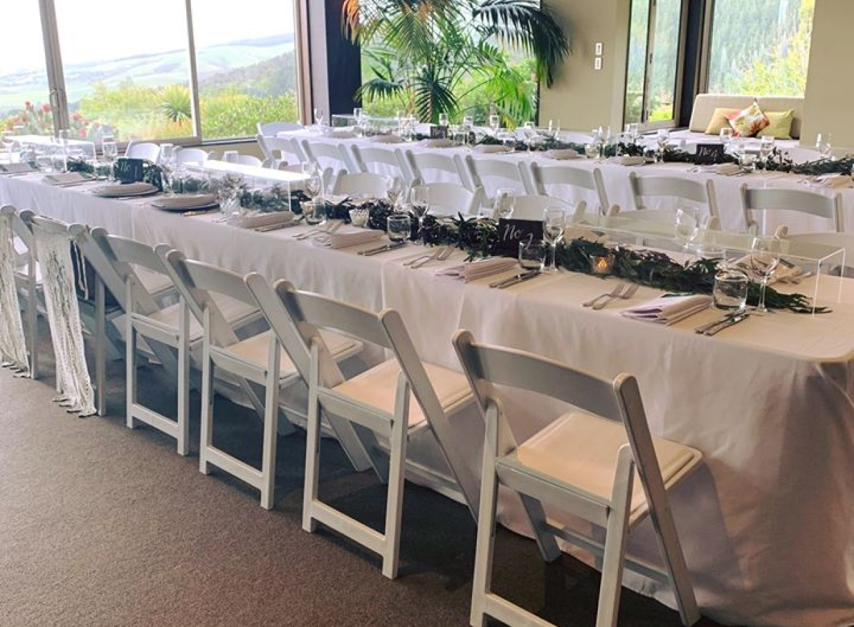 Waipuna Estate's elegant, modern reception room in Christchurch, set with banquet tables, overlooks scenic views.
