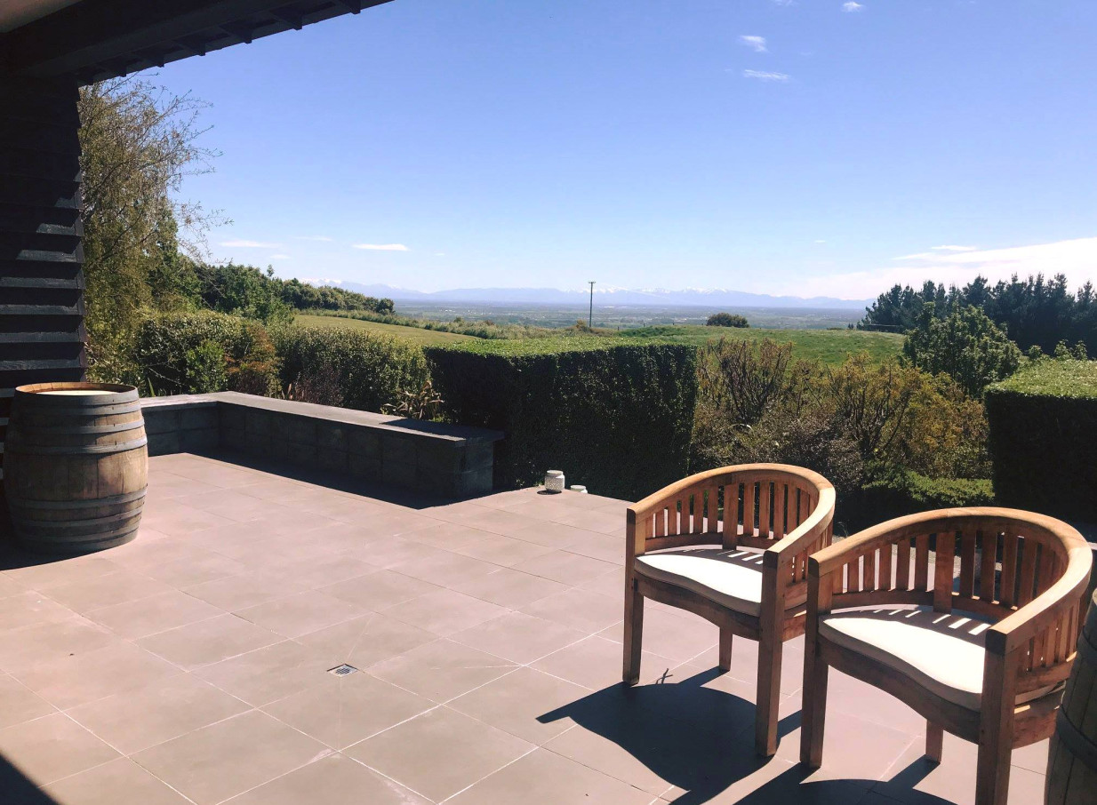 Waipuna Estate, a luxurious modern villa in Christchurch, presents an outdoor patio with panoramic views of the natural landscape.