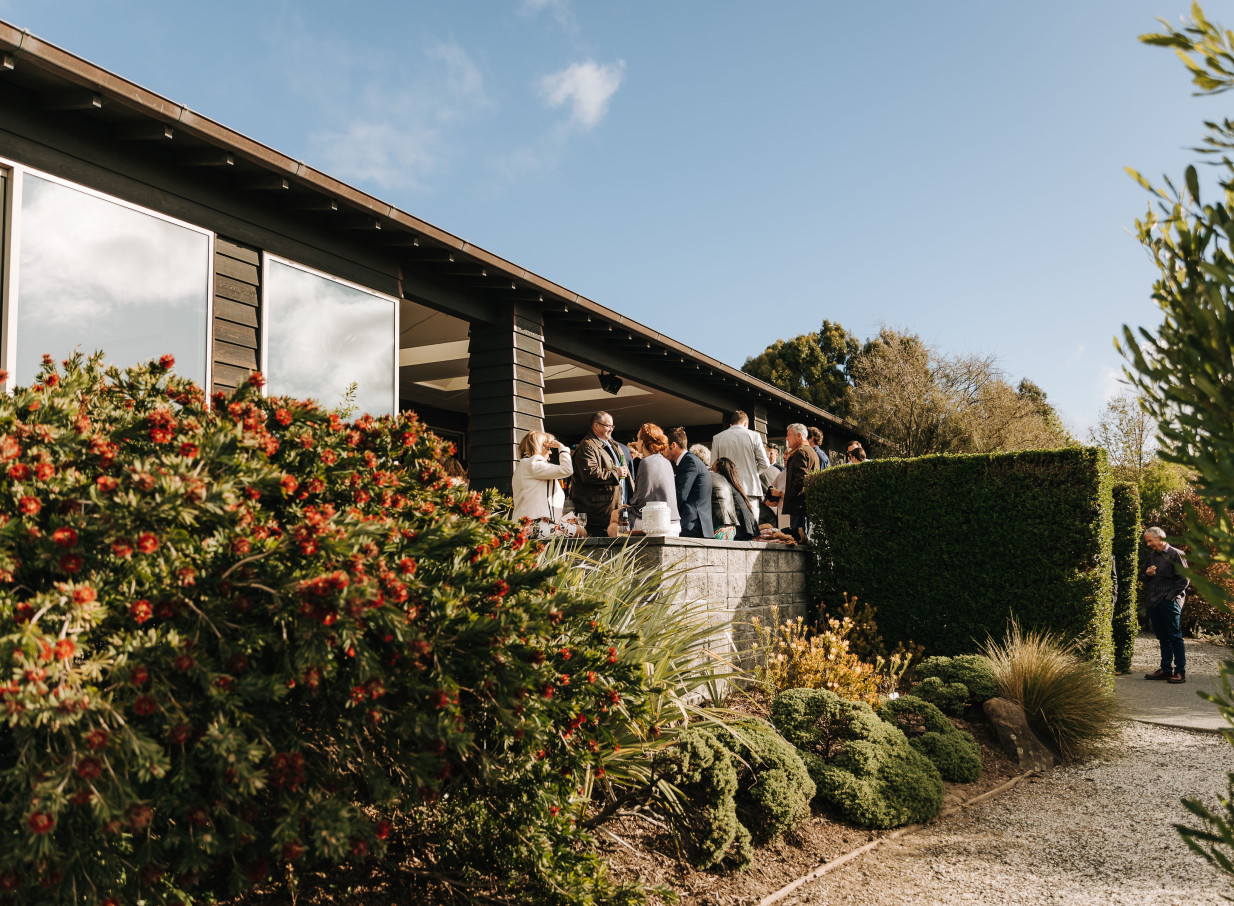 Guests mingle on the modern contemporary covered terrace at Waipuna Estate, Christchurch, framed by lush gardens.