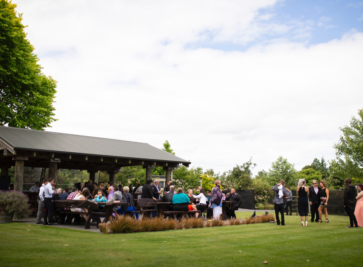 An outdoor gathering under a rustic covered pergola with wooden tables at Omarino Estate, Christchurch.