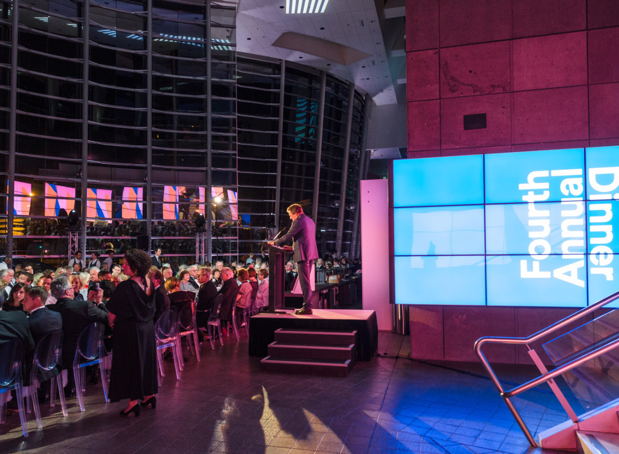 A 'Fourth Annual Dinner' event takes place in the modern, flowing glass interior of Christchurch Art Gallery Te Puna o Waiwhetū.