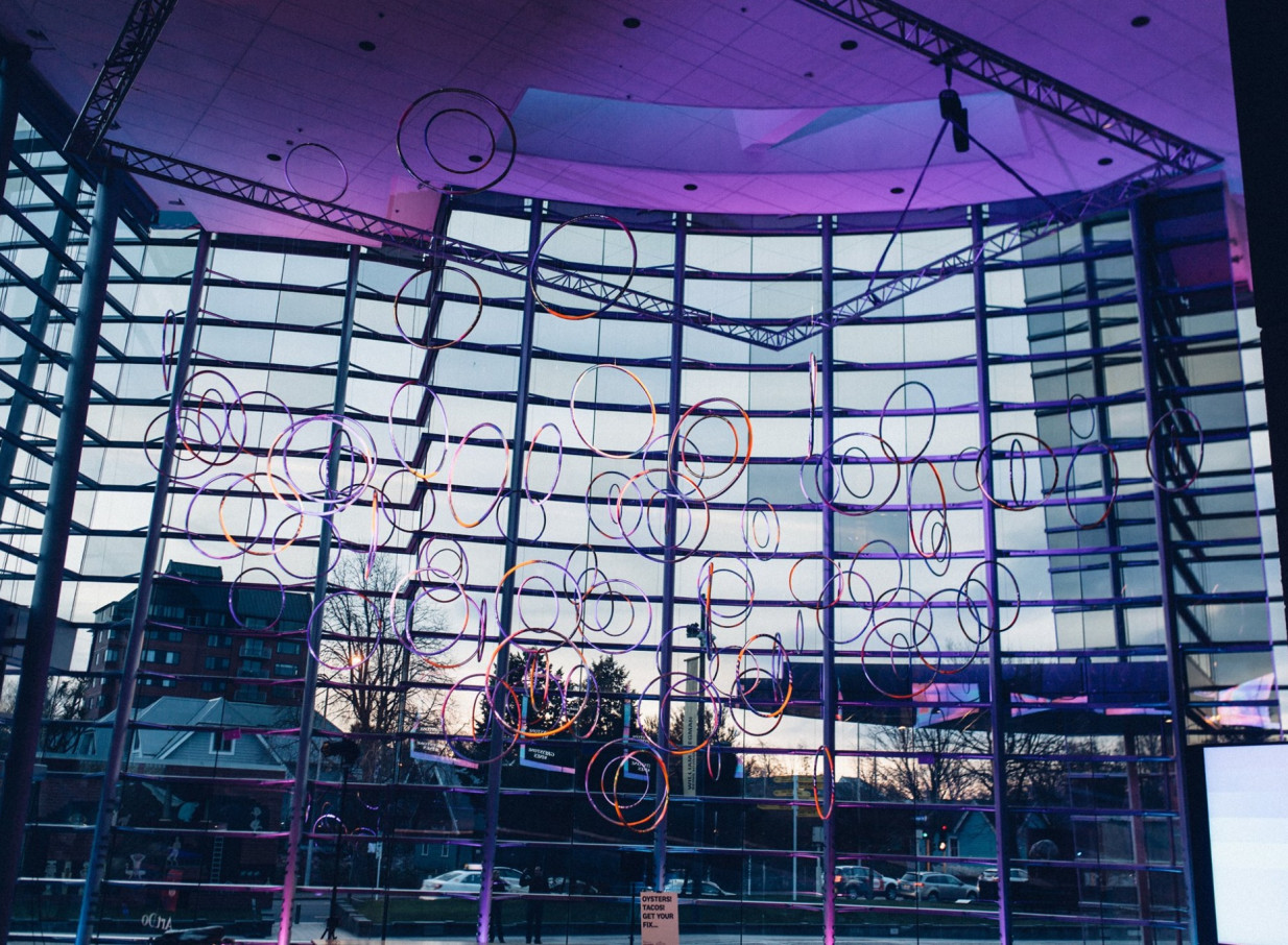 Inside Christchurch Art Gallery Te Puna o Waiwhetū's modern glass foyer, illuminated circular art hangs before an undulating glass facade.