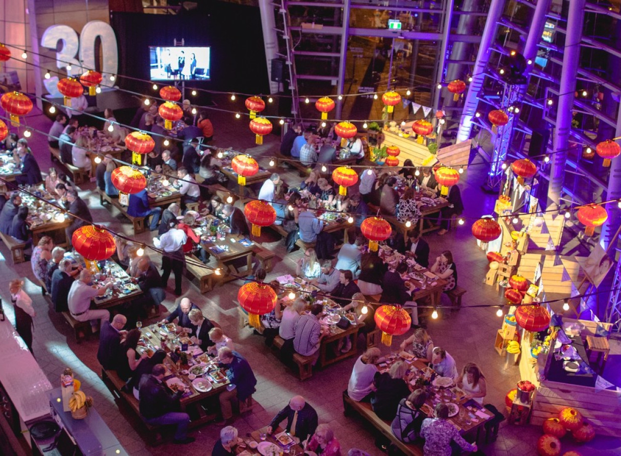 A festive dining event under red lanterns and string lights in the modern glass atrium of Christchurch Art Gallery Te Puna o Waiwhetū.