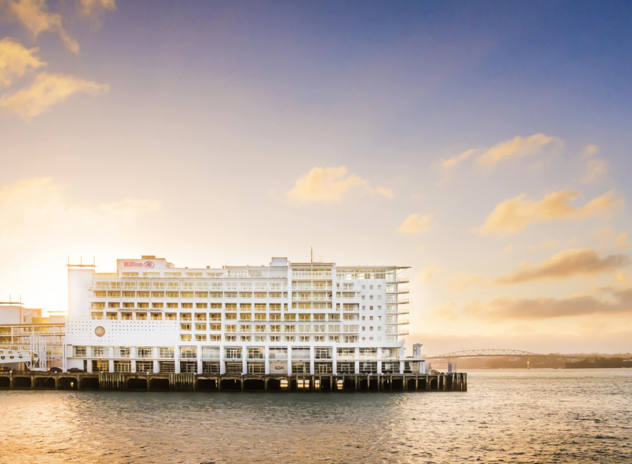 An exterior view of the contemporary, nautical-inspired Hilton Auckland hotel on Princes Wharf at sunset.