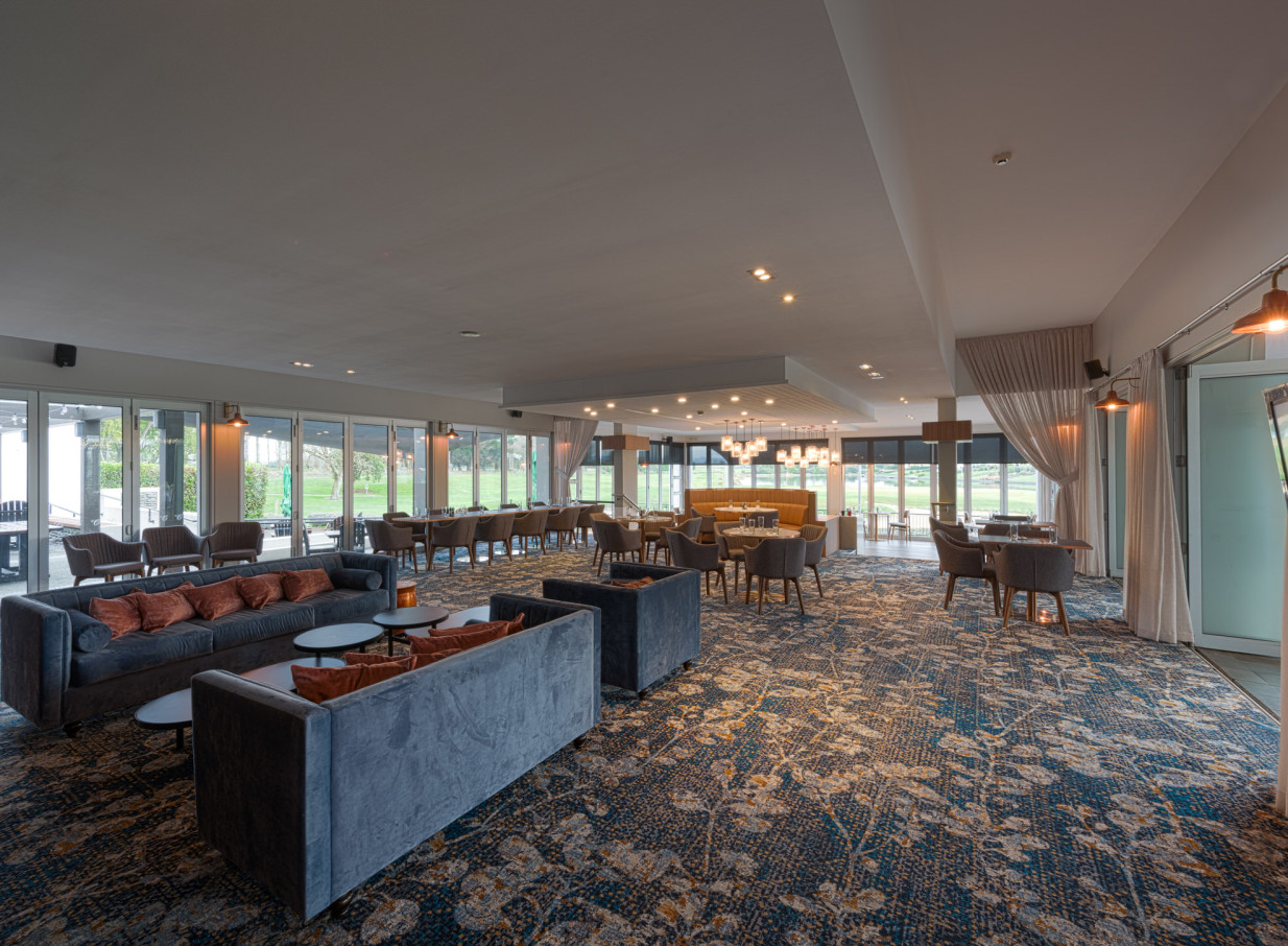 The contemporary dining and lounge space at Peppers Clearwater Resort, Christchurch, features elegant furnishings and floor-to-ceiling windows overlooking lush grounds.