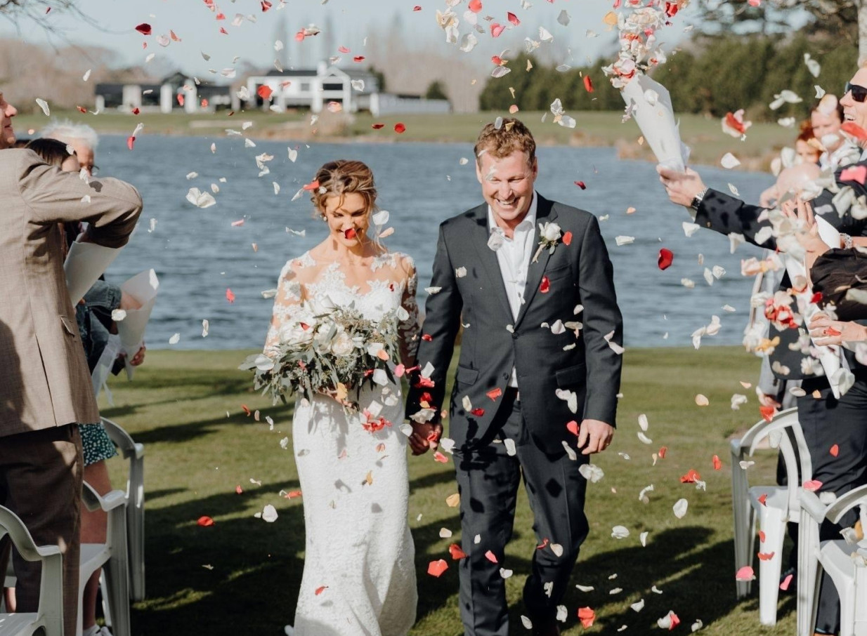 A joyful outdoor wedding celebration with petals falling on the couple at the elegant, lakeside Peppers Clearwater Resort in Christchurch.